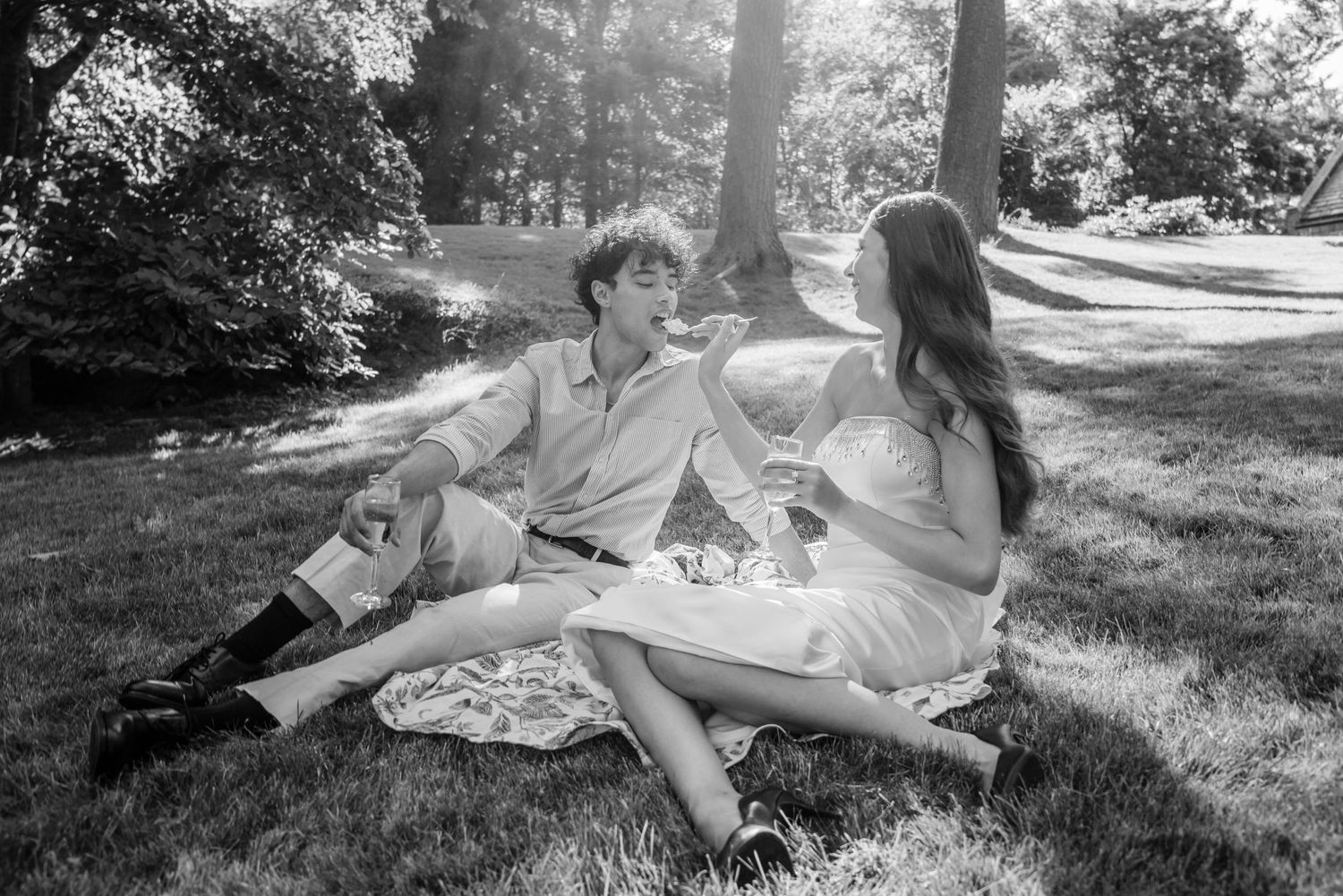 Black and white photo of couple having picnic on grass in park setting.
