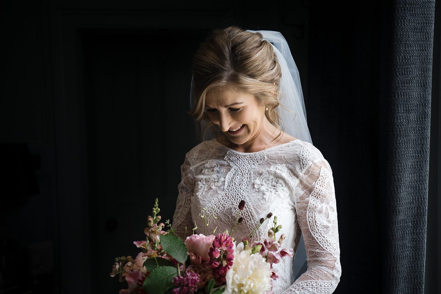 A Westin Nova Scotian Hotel bride in a long-sleeve lace wedding dress holding a pink and white floral bouquet while laughing.