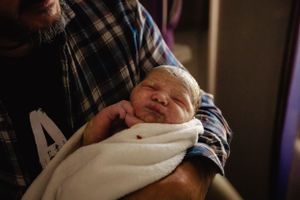 A tender moment of skin-to-skin contact with a newborn swaddled in white fabric.