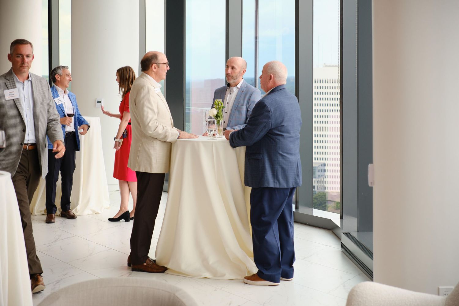 Small group gathered around cocktail table at networking event with city views.
