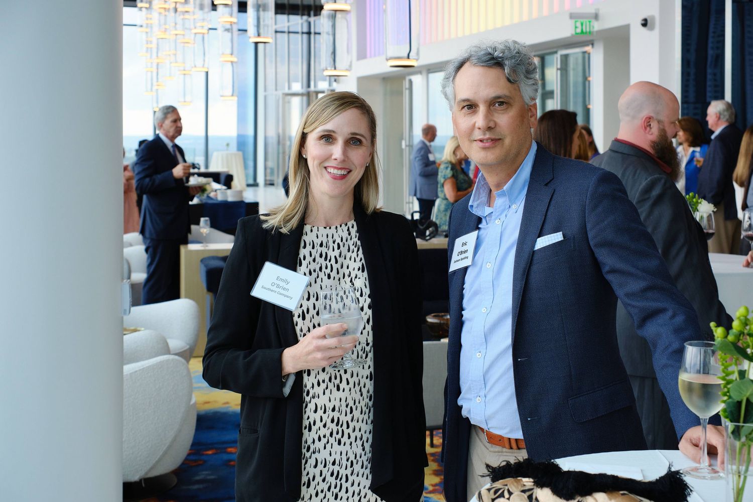 Networking event participants standing in modern venue with city backdrop.
