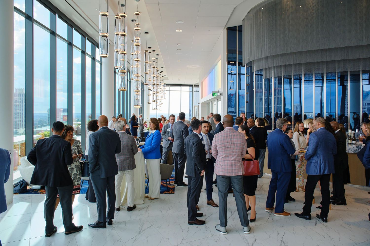 Business networking event with attendees gathered in small groups throughout a modern windowed space.