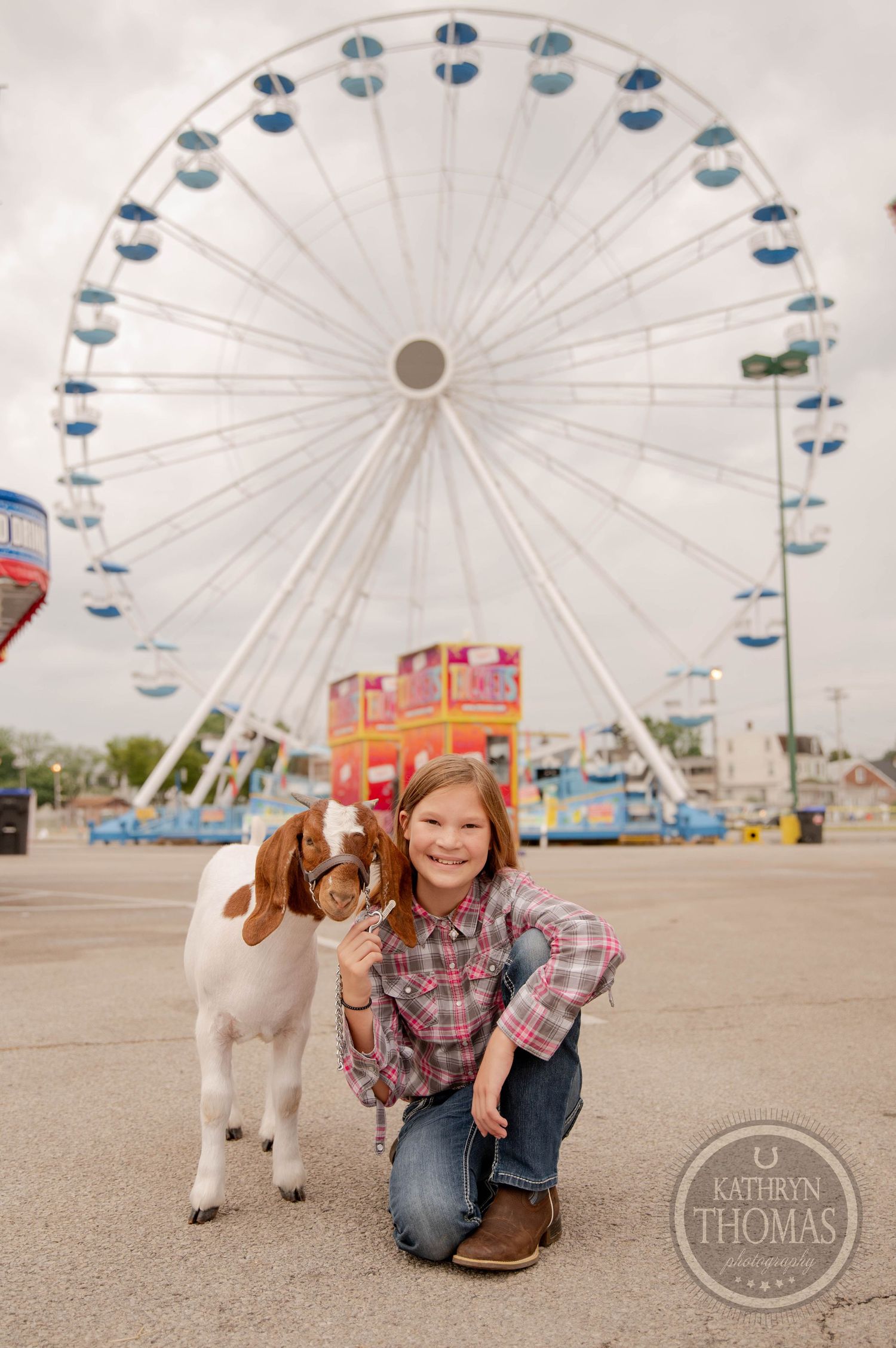 White and brown goat stands with handler in front of large ferris wheel at county fair.