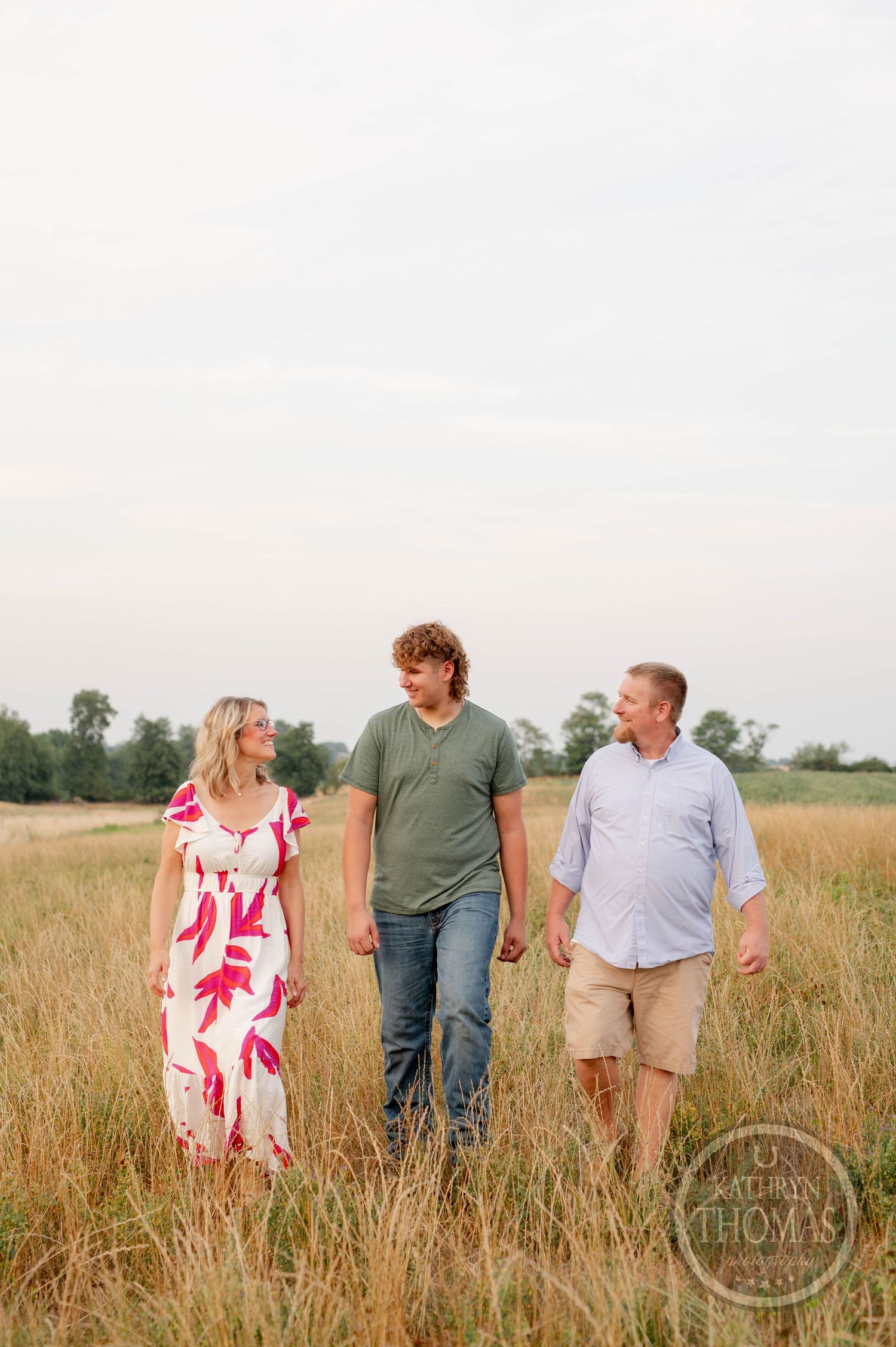 Three people walking and smiling in a golden wheat field during sunset.