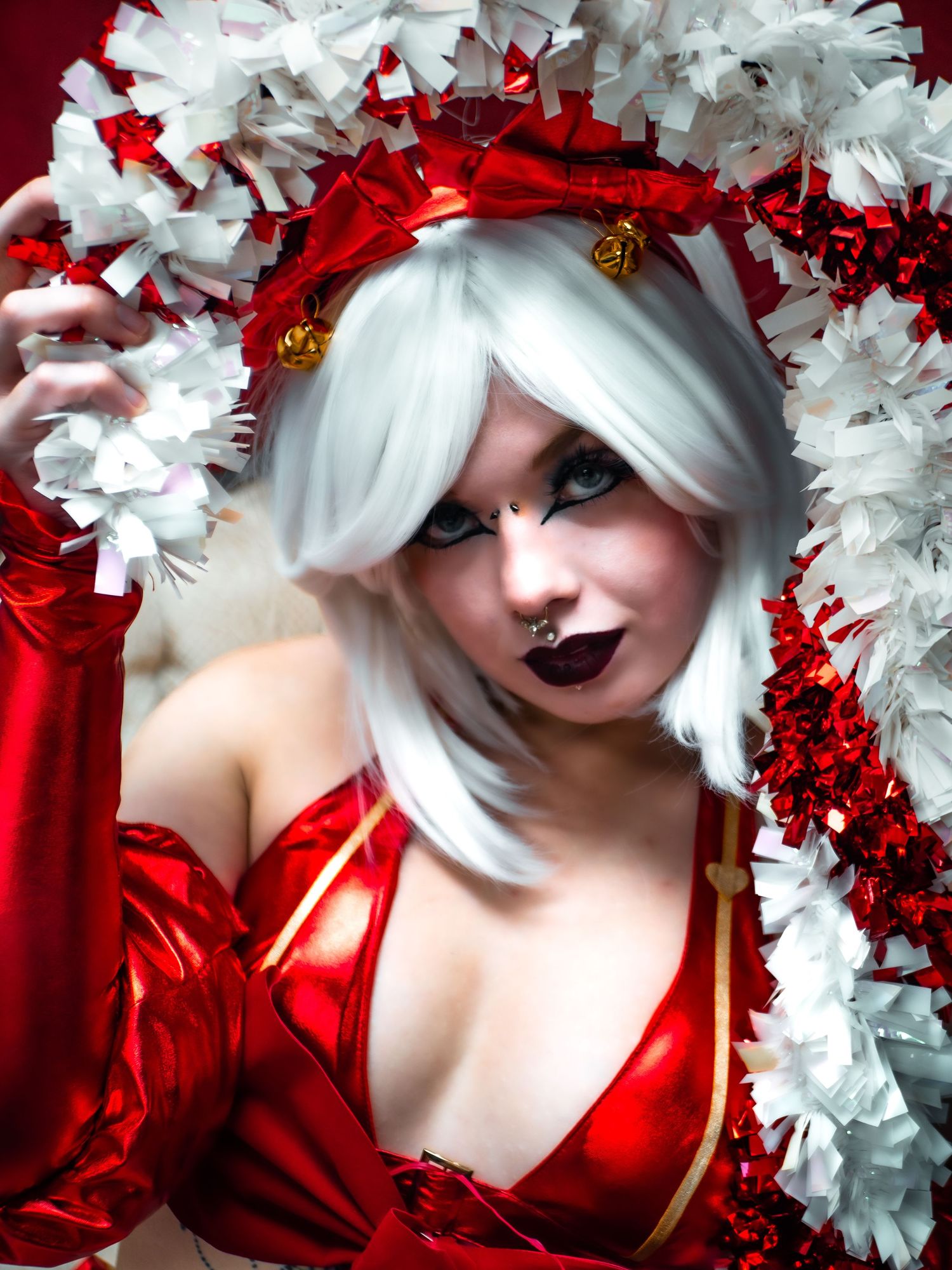 Red and white cosplay outfit with silver wig and dramatic gothic makeup against white and red decorative background.