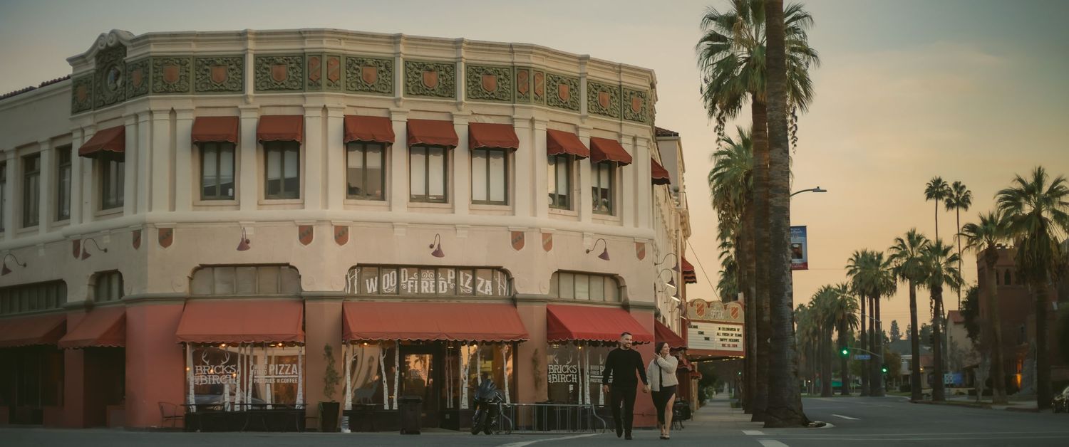 Vintage style architecture of a corner restaurant with red awnings and palm trees along the downtown Redlands street at sunset.