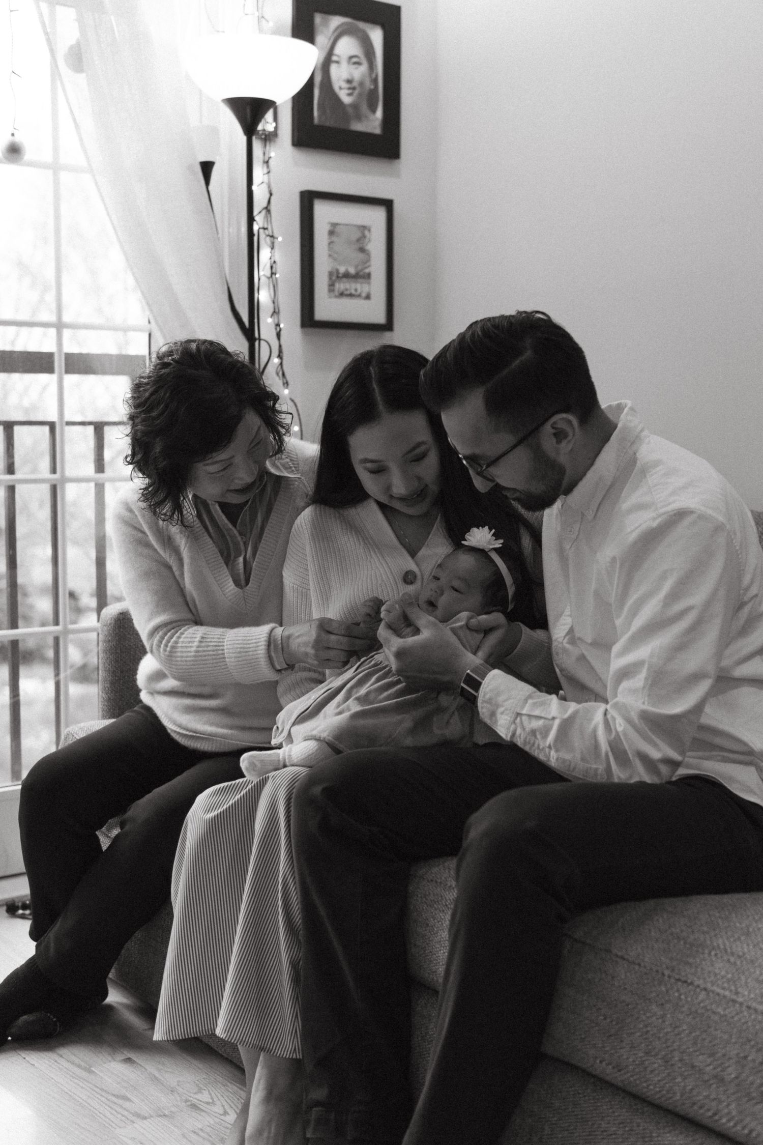Black and white photograph showing a family gathered on a couch spending time with a newborn at newborn photoshoot.