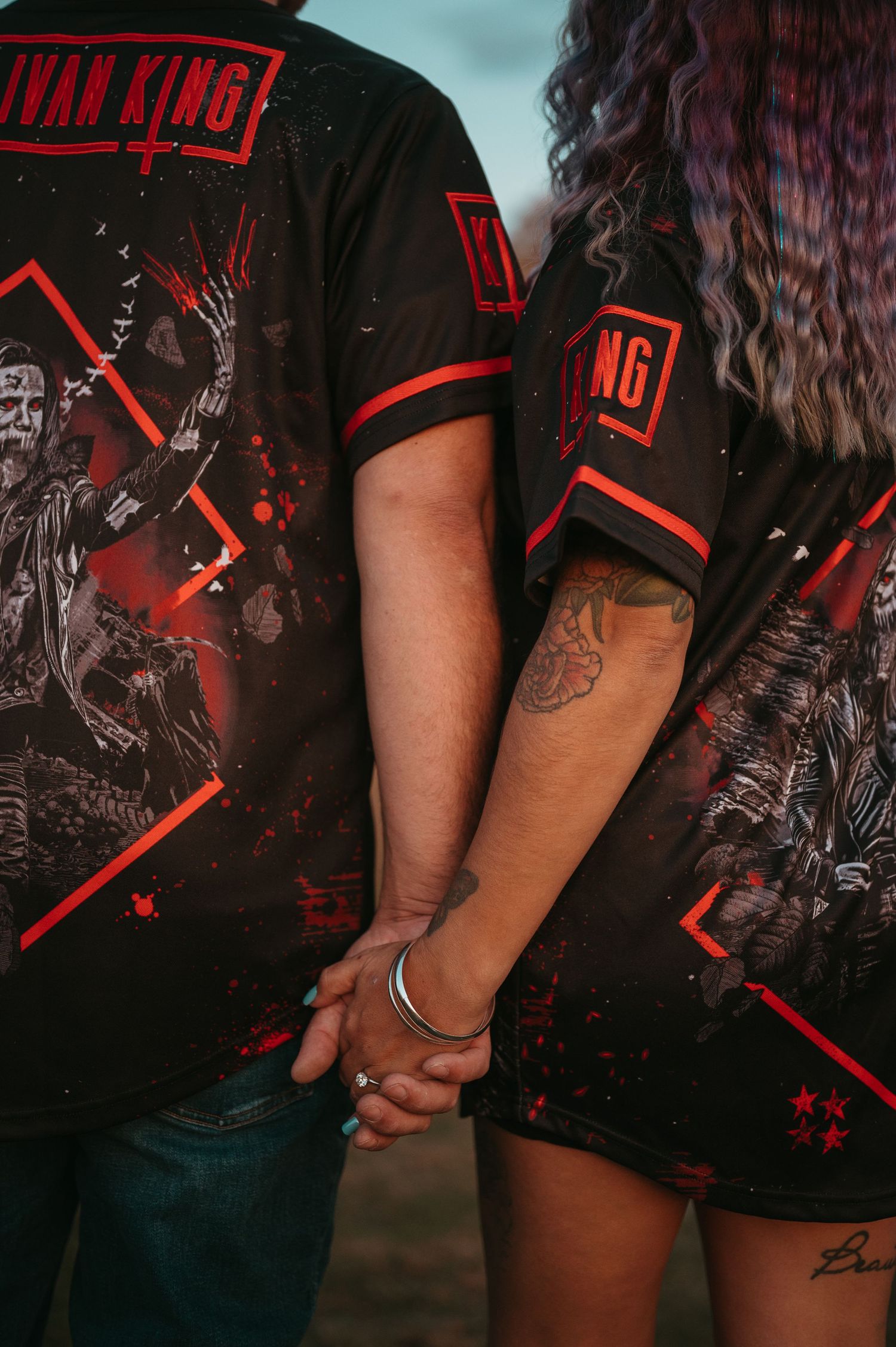 Close up of couple wearing matching black and red band t-shirts holding hands.
