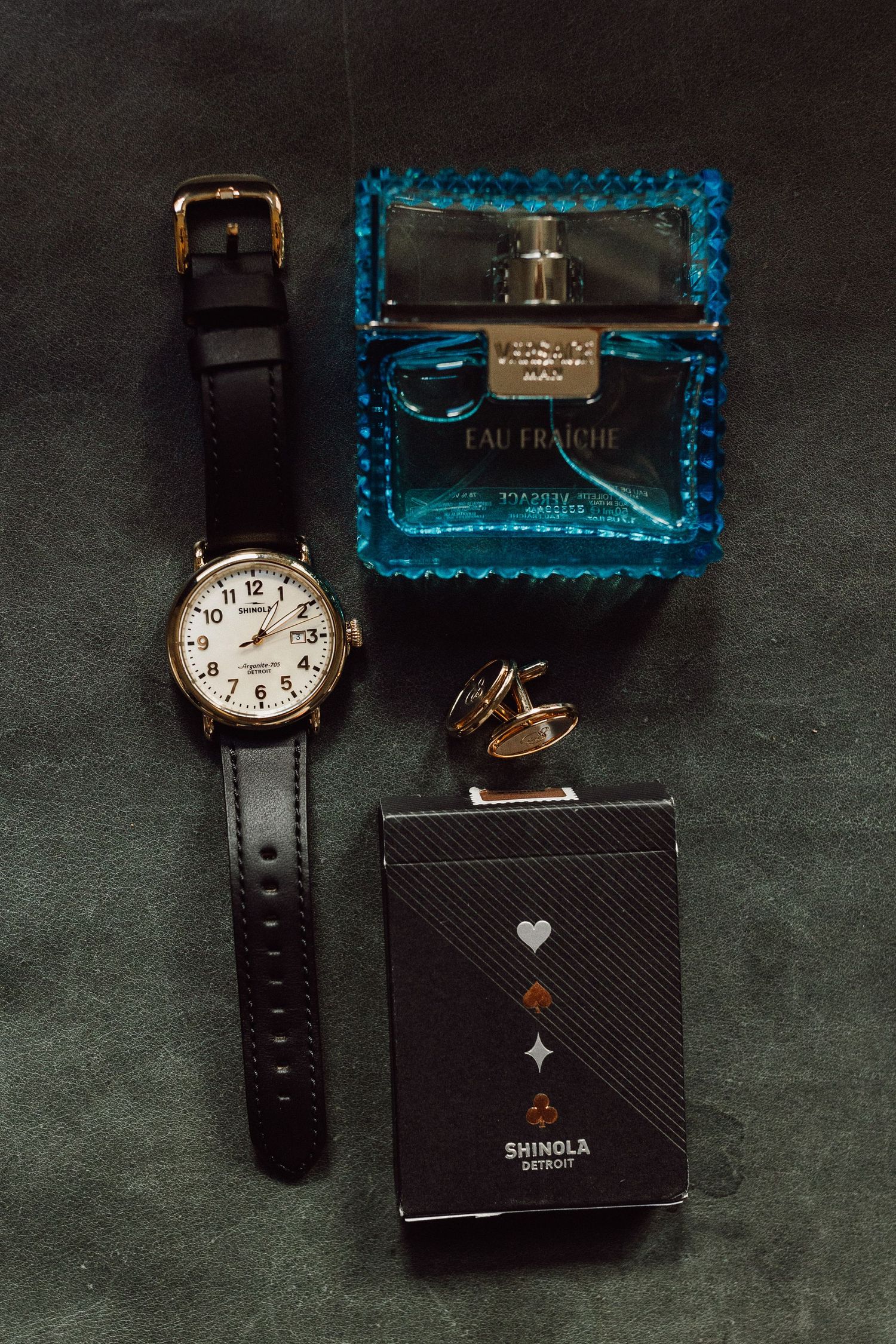Luxury accessories including watches, cufflinks, and blue cologne bottles arranged on dark textured surface.