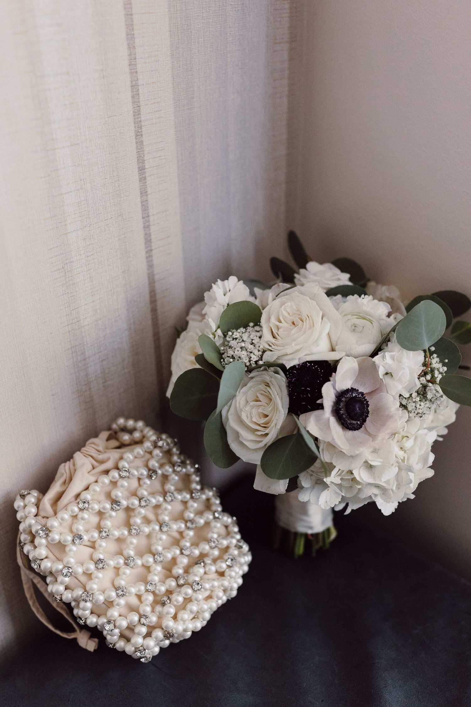 Wedding accessories including pearl clutch, white roses and anemone flower bouquet.