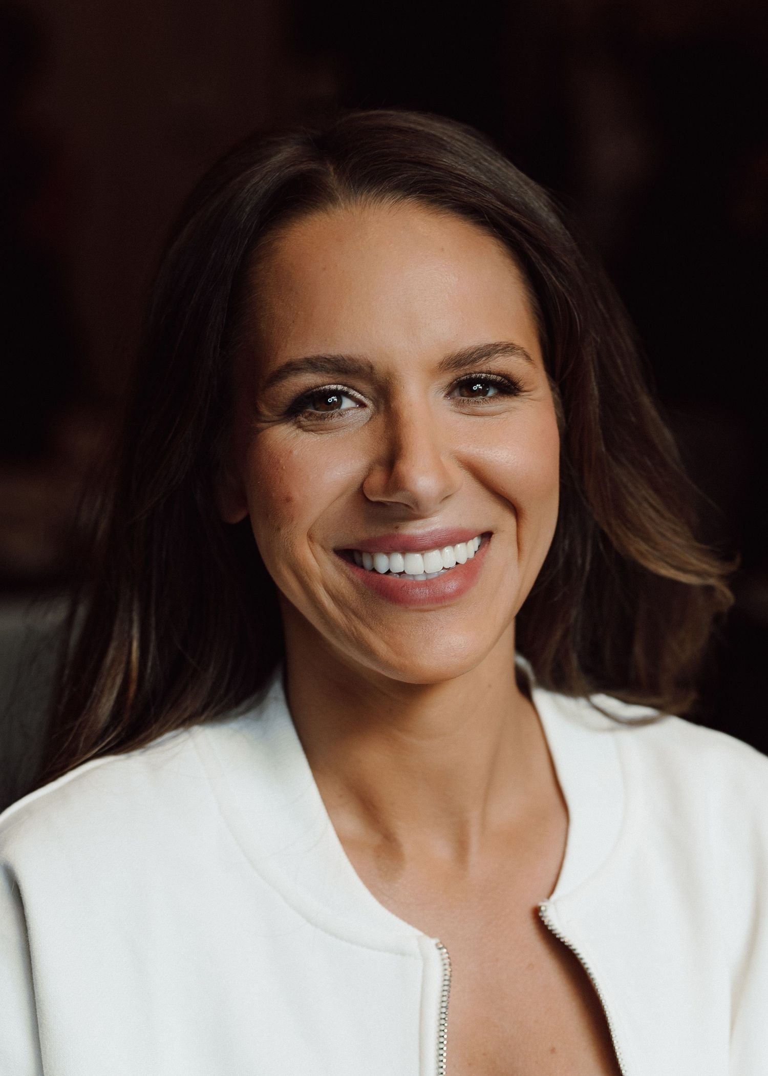 Portrait of someone in white wearing natural makeup and showing a bright smile.