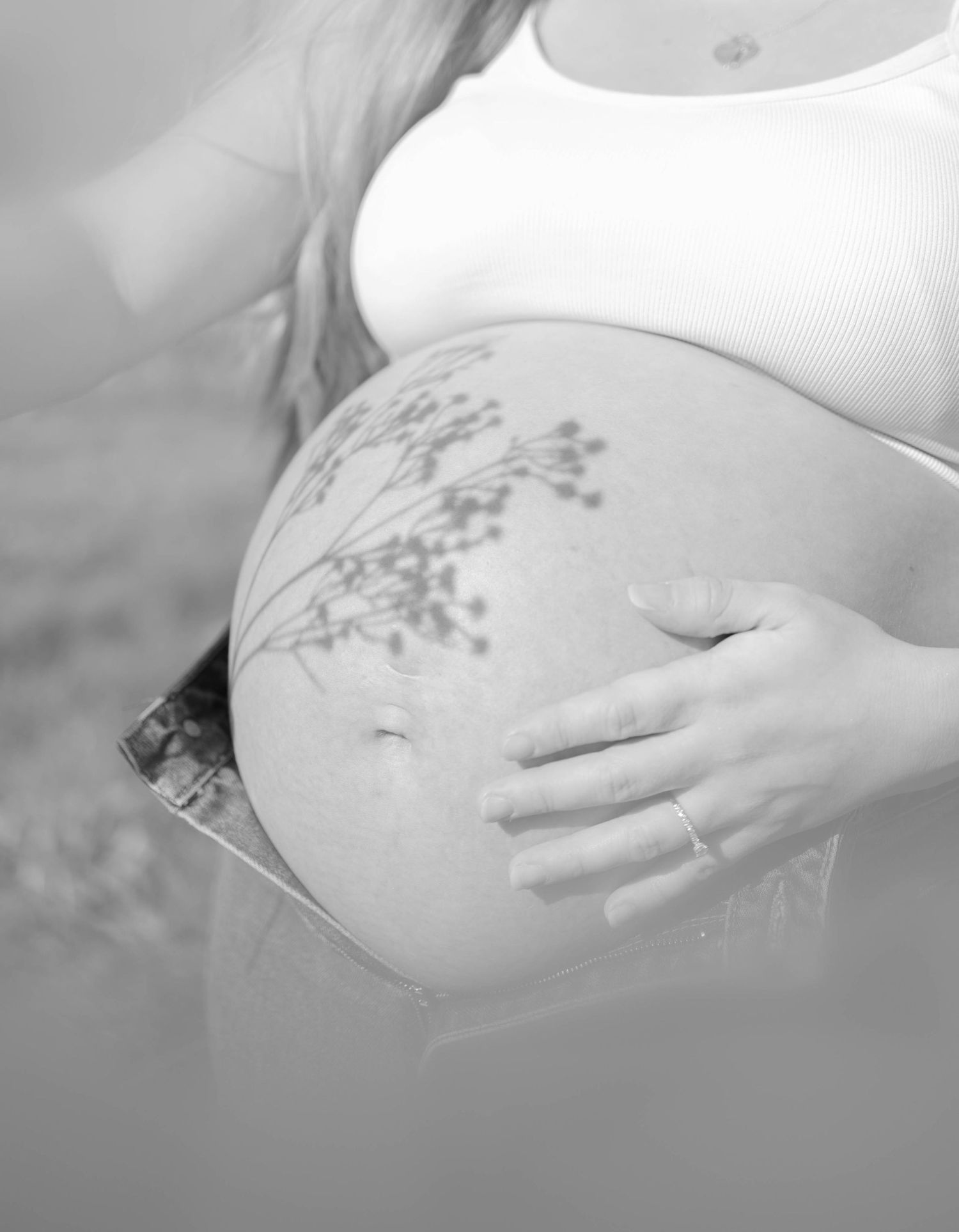 Black and white photo of pregnant belly with floral tattoo and hand resting on bump.