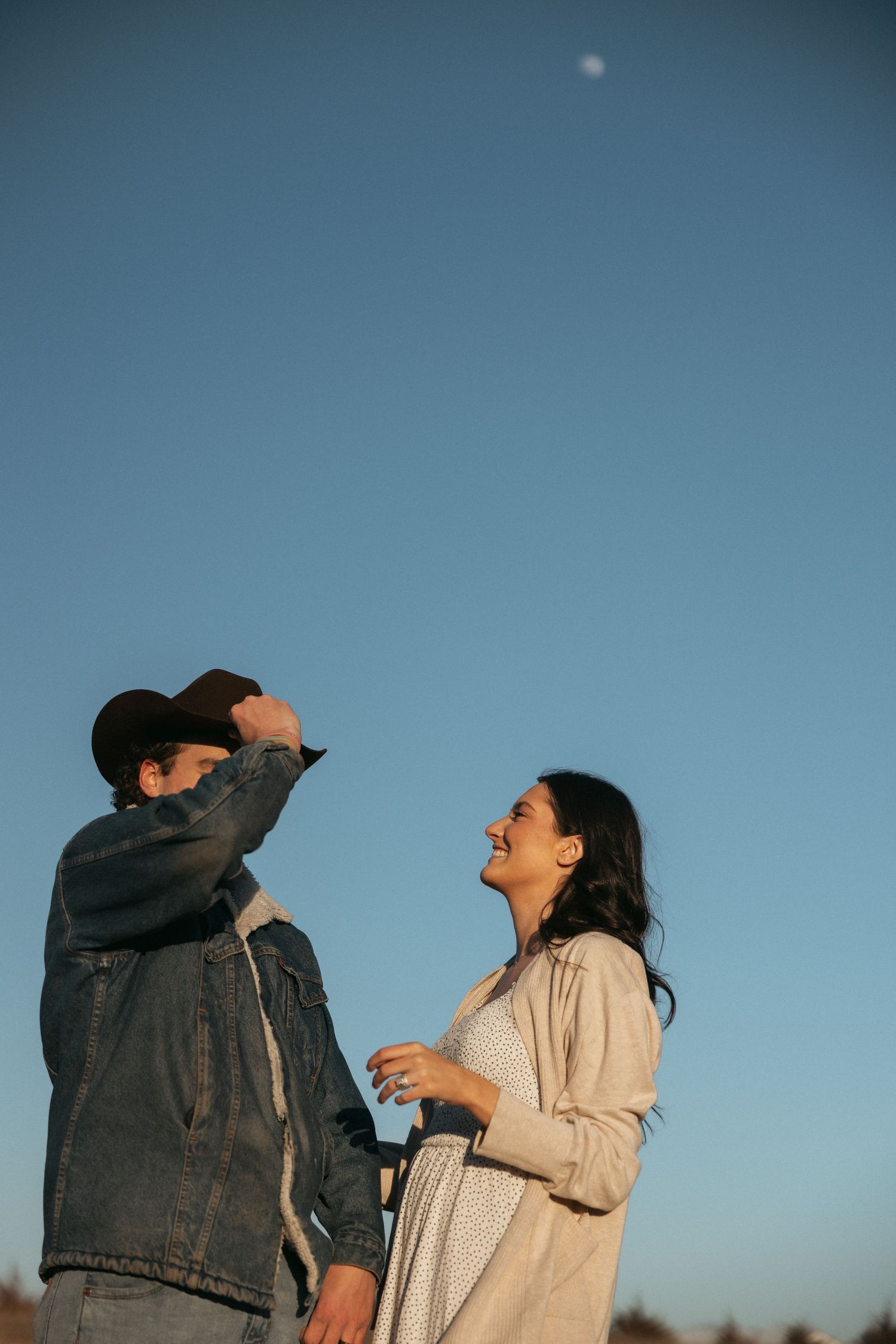 Two people share a joyful moment outdoors against a blue sky with one reaching up and laughing.