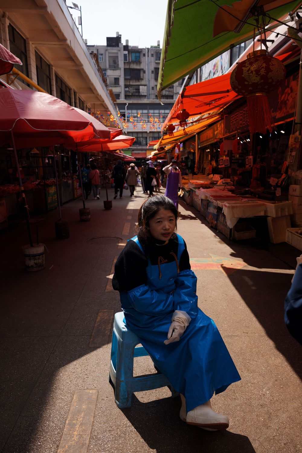 A covered market street in Hong Kong with red awnings and vendor stalls while someone sits on a stool.