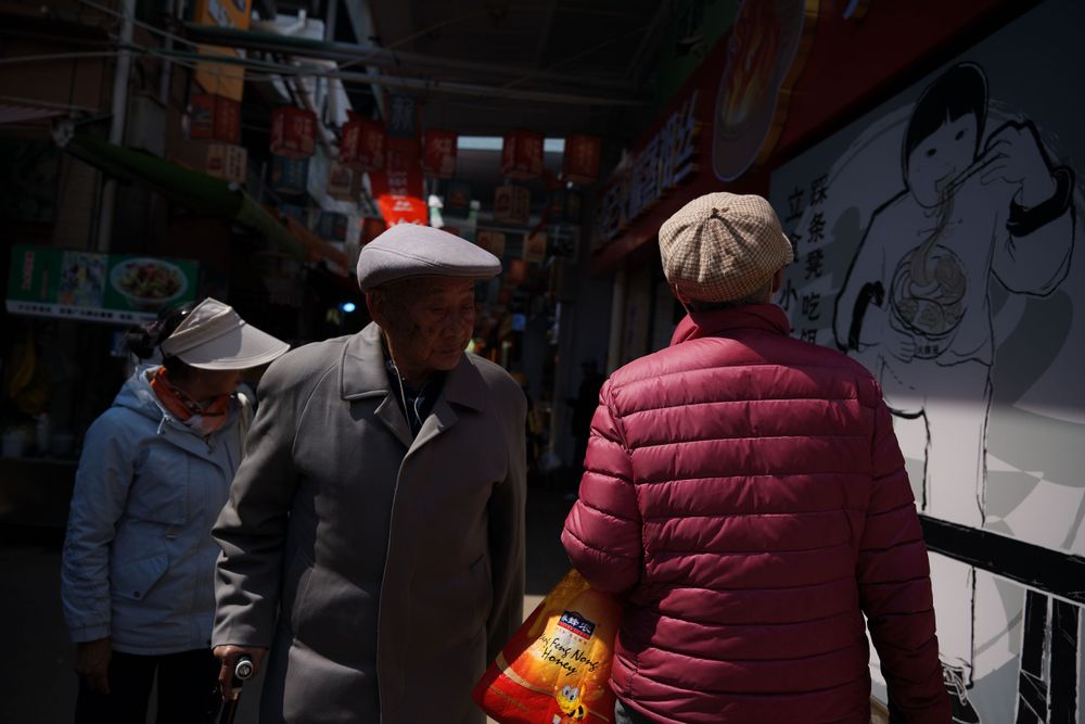 People wearing winter coats walk through a covered market alley with graffiti walls and shadows creating contrast.