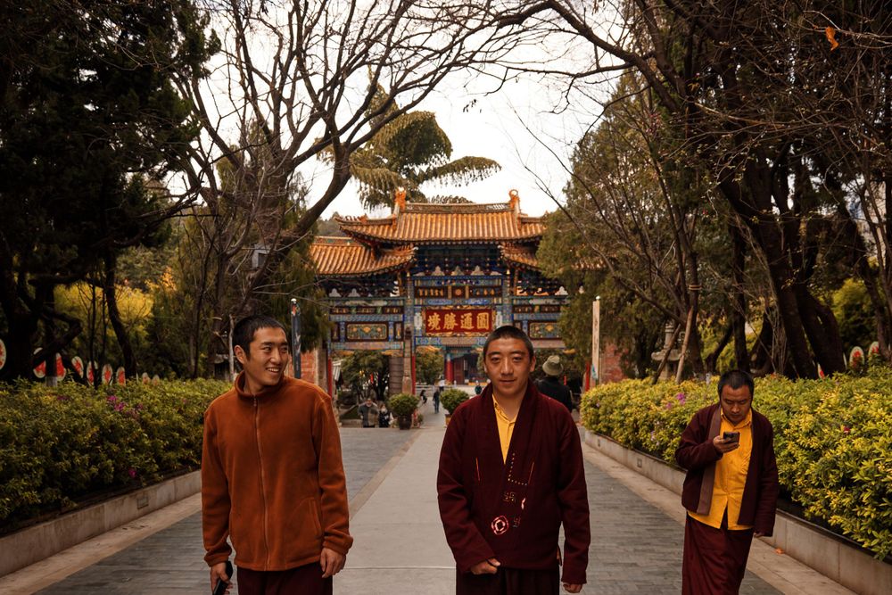 People stand on a path leading to a traditional Chinese temple gate with ornate architecture and decorative details.