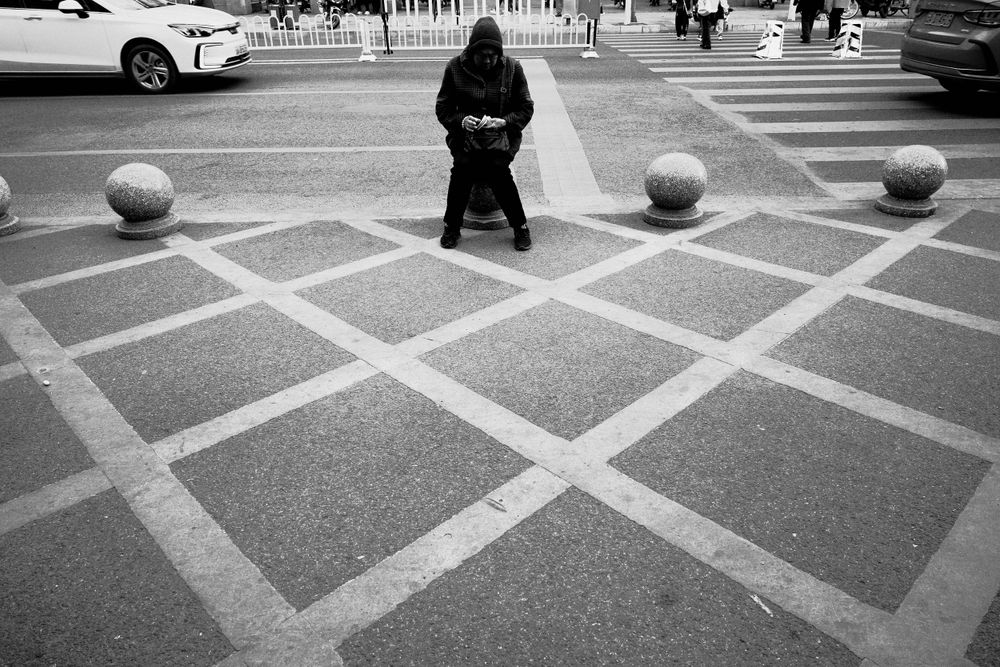 A person sits alone on a geometric patterned plaza with concrete spheres and white lines on the ground.