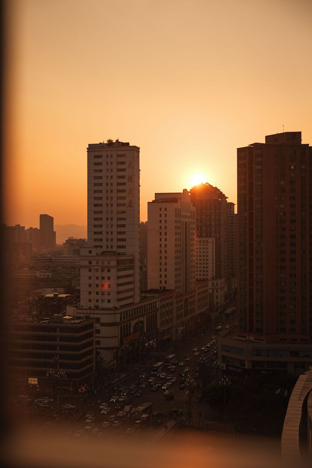 Sunset silhouettes tall apartment buildings and city skyline with golden sunlight casting long shadows over urban street.