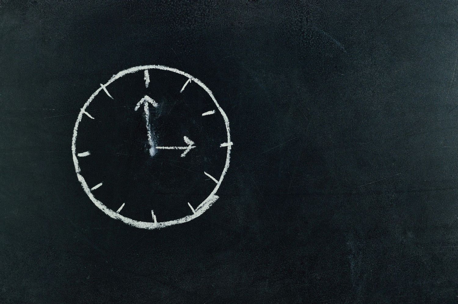 Simple clock face drawing sketched in white chalk on a dark chalkboard showing quarter past two.