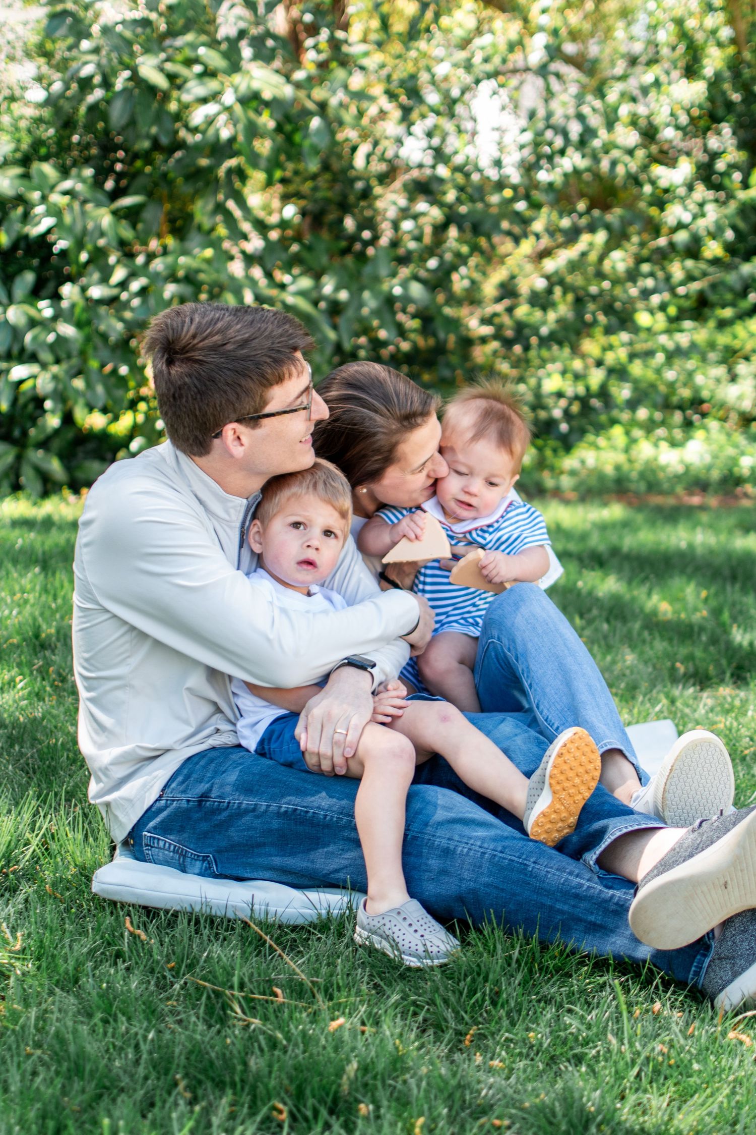 A family sits together on green grass in a sunny garden, enjoying a relaxed outdoor moment on a warm day.