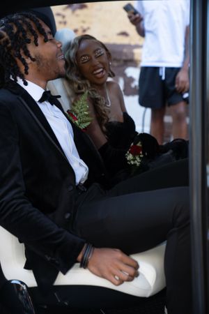 Couple in formal attire sharing a joyful moment in luxury car with white interior.