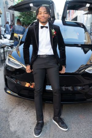 Person wearing velvet tuxedo and bow tie standing in front of black Tesla Model X.