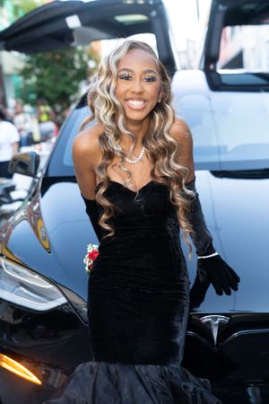 Stunning black mermaid gown with velvet top and long evening gloves in front of a Tesla.