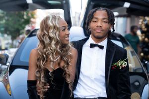 Formal couple in black tie attire posing in front of a luxury Tesla vehicle.