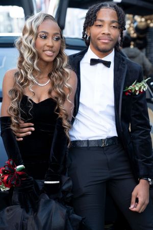 Elegant prom couple in matching black formal wear posed by luxury vehicle.