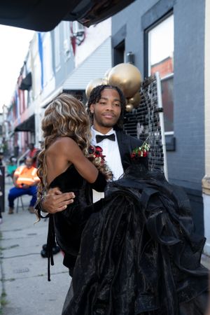 Couple shares intimate moment in formalwear on city sidewalk next to decorated venue.