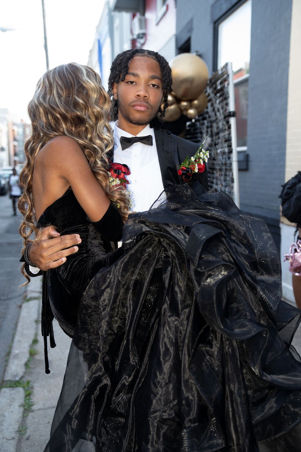 Couple in formal attire embracing at a prom event with black and gold decor.