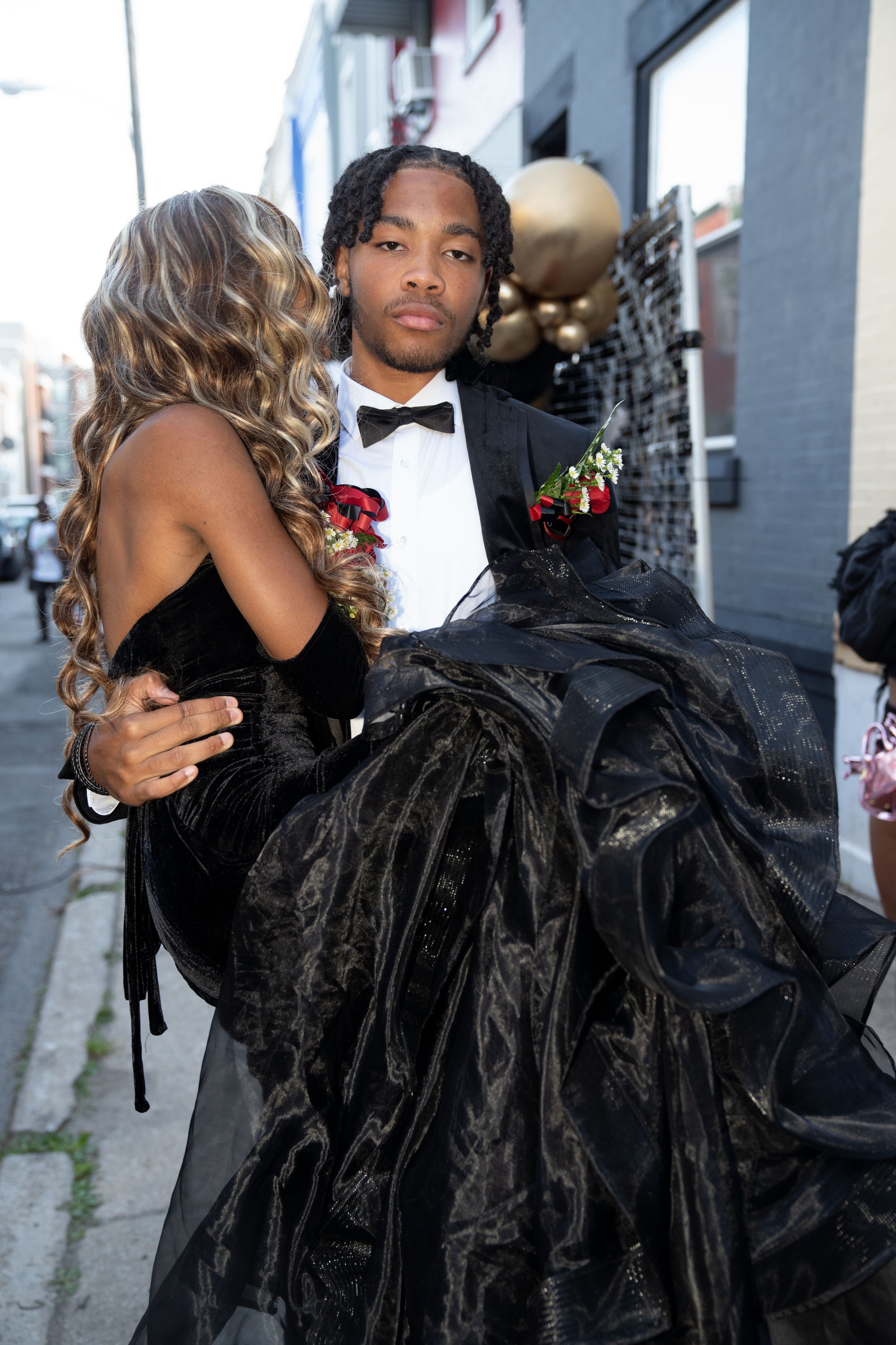 Couple in formal attire embracing at a prom event with black and gold decor.