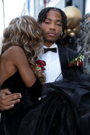 Close-up of formal couple embracing against urban backdrop with decorative lighting.
