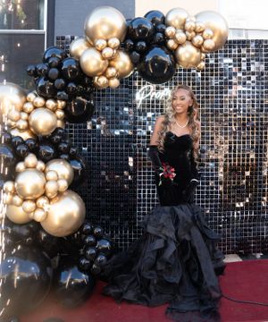 Formal event photo backdrop with black and gold balloon arch and red carpet.