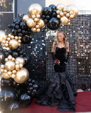 Glamorous pose against sparkly backdrop with gold and black balloon decorations.