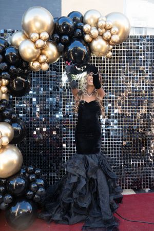 Full-length shot of black mermaid gown against sparkly backdrop with balloon arch.