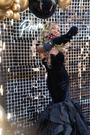 Dramatic pose in black velvet mermaid gown against sequined wall with balloon decor.