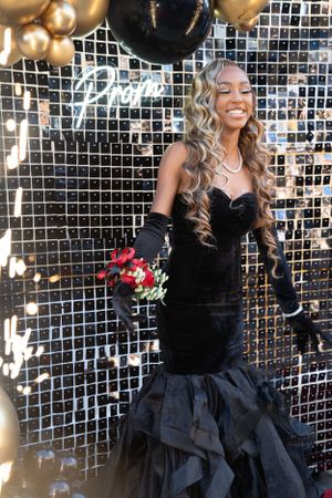 Elegant mermaid-style black velvet gown with ruffled skirt photographed against a sparkly backdrop with gold balloons.