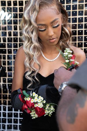 Elegant prom dress photo featuring black velvet gown with pearl necklace and red rose corsage against mosaic backdrop.