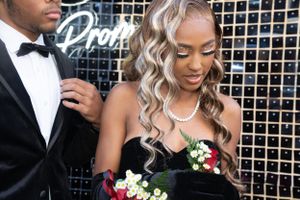 Formal couple poses against sparkly backdrop with black gown and tuxedo at prom event.