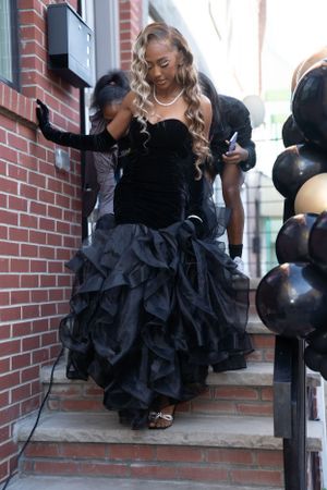 Sweetheart neckline black ball gown with ruffled skirt descending brick stairs with black balloons.