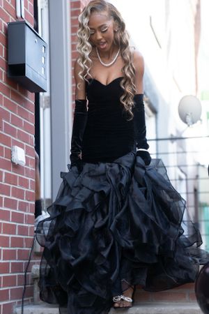 Long black velvet gown with dramatic ruffled skirt and elegant pearl necklace on brick steps.
