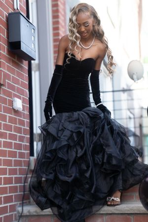 Strapless black velvet gown with layered ruffled skirt and long gloves on brick entrance.