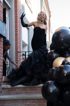 Joyful moment in black formal gown on brick steps decorated with black balloons.
