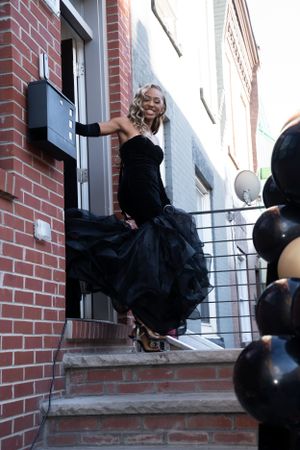Dramatic black ball gown photographed on brick steps with urban backdrop.
