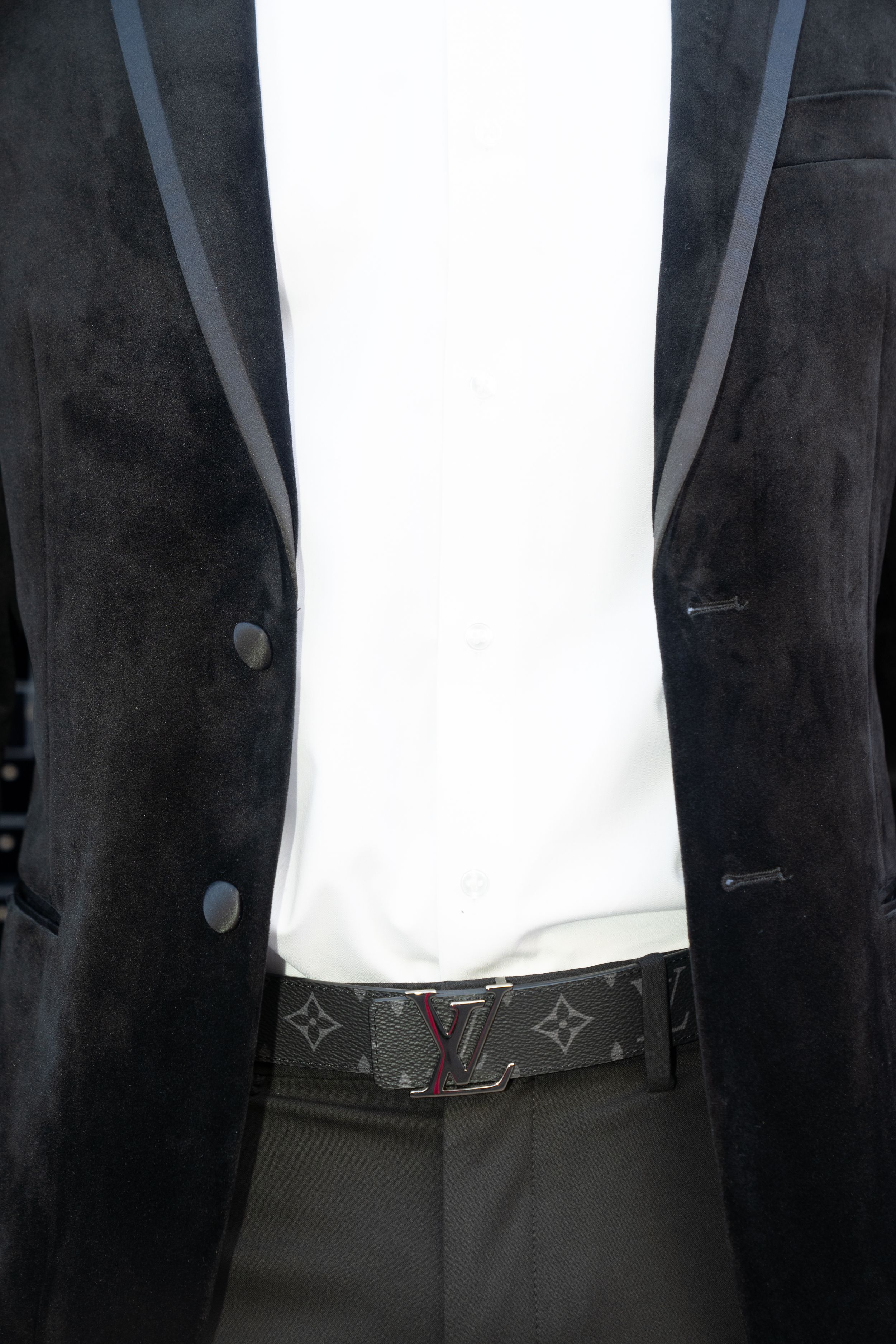Close-up of a black velvet suit jacket with a Louis Vuitton belt visible at the waist.