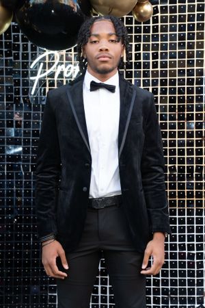 Formal portrait against a sparkly backdrop wearing black velvet tuxedo and bow tie.