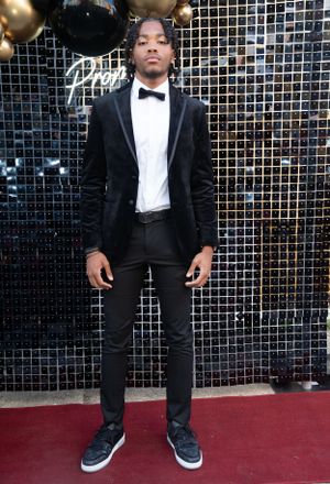 Full-length photo showing elegant black tuxedo with casual sneakers on a red carpet.