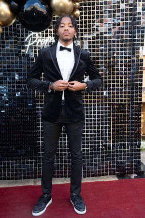 Stylish formal portrait in black tuxedo against metallic backdrop with balloons.