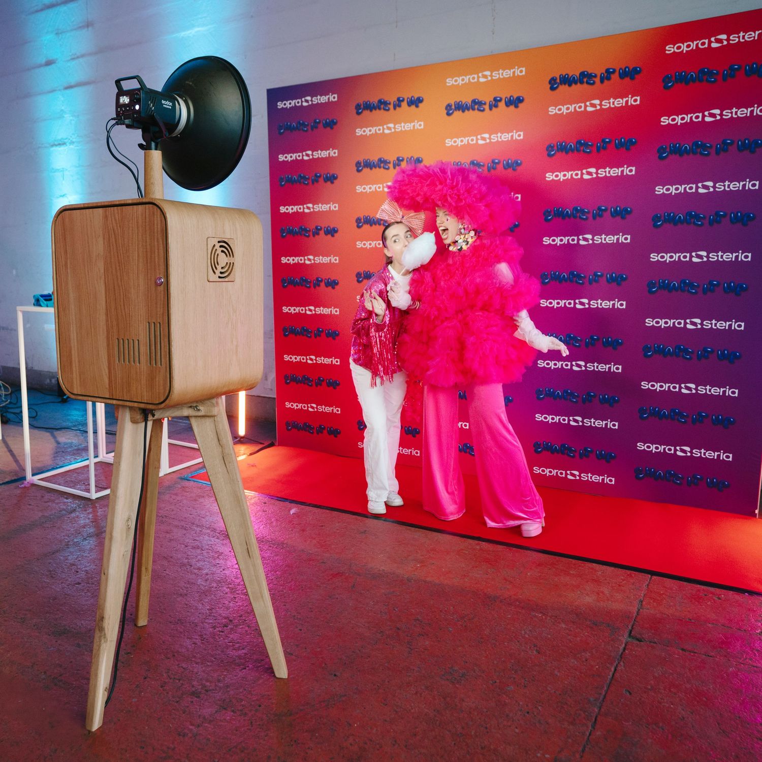 Vintage wooden photo booth camera on tripod with two people in bright pink costumes posing.